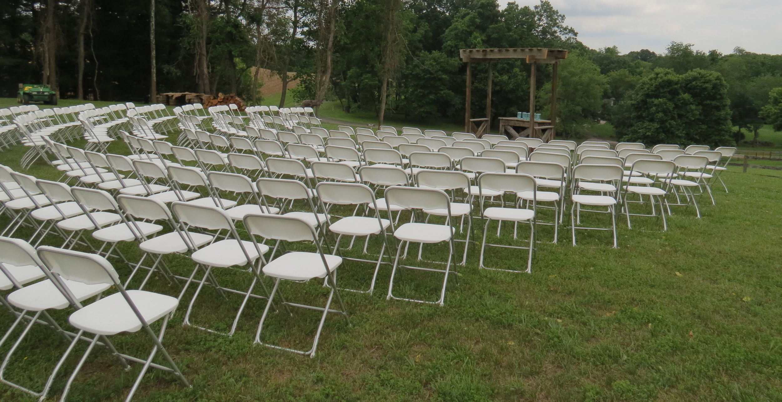 Outdoor wedding setup featuring rows of white folding chair rentals from Bee Ready Rentals, perfect for ceremonies and gatherings.